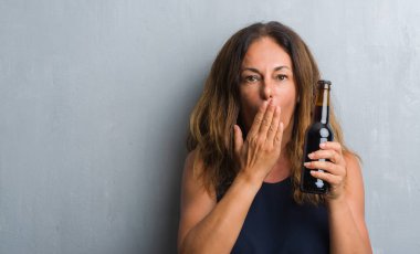 Hata, korku, sessizlik içinde gizli kavramı korkmuş ifade için utanç ile bira şişe kapağı ağız eliyle tutarak gri grunge duvarın üzerinden duran orta yaş İspanyol kadın şok