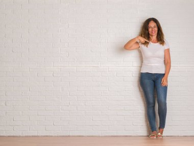 Sürpriz yüz işaret parmağı beyaz tuğla duvarın üzerinden kendisine duran orta yaş İspanyol kadın