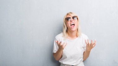 Yetişkin beyaz kadın çılgın ve kızgın bağırarak ve agresif ifade ve silah kaldırdı bağırmaya güneş gözlüğü takıyor grunge gri duvar yüzünden. Hayal kırıklığı kavramı.