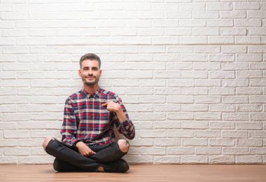 Sürpriz yüz işaret parmağı kendisine beyaz tuğla duvar oturan genç yetişkin adam