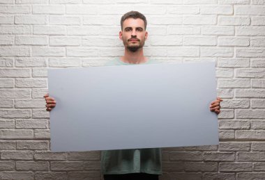 Genç yetişkin adam afiş kendine güvenen bir ifade ile acımak yüz ciddi düşünüyorum tutarak tuğla duvarın üzerinden