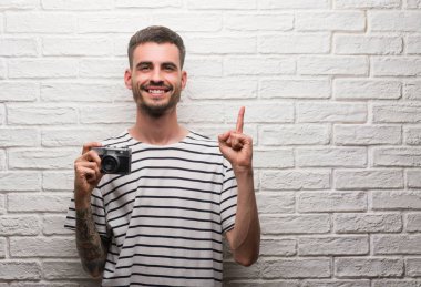 Genç adam beyaz tuğla duvarın üzerinden vintage fotoğraf makinesi ayakta tutan bir fikir ya da soru işaret parmağı gülen yüz, bir numara ile şaşırttı