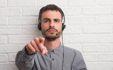Genç yetişkin adam kamera ve size parmak ile işaret operatörü olarak çalışan tuğla duvarın üzerinden, el işareti, pozitif ve kendinden emin bir jest ön