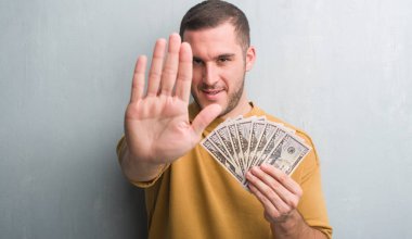 Genç beyaz adam açık eliyle dur işareti ile ciddi ve kendine güvenen ifade, savunma jest yapıyor dolar tutan gri grunge duvarın üzerinden