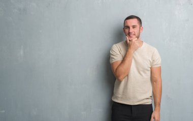 Beyaz delikanlı emin çapraz kollar ve çeneme kaldırdı el ile gülümseme ile kamera seyir gri grunge duvarın üzerinden. Pozitif düşünce.