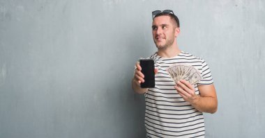 Dolar ve smarphone görünümlü yan ve dik dik bakma uzağa düşünce gülümseyen tutan gri grunge duvarın üzerinden beyaz delikanlı.