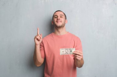 Gri grunge Genç beyaz adam gösteren beş dolar bir fikirle sürpriz duvar veya gülen yüz, bir numara ile işaret parmağı soru