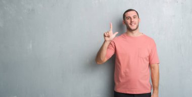 Beyaz delikanlı gösterilen ve parmakları ile işaret gri grunge duvarın üzerinden ikincisi ise kendinden emin ve mutlu gülümseyerek.