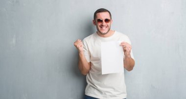 Duygu tezahürat Genç beyaz adam gurur çığlık ve zafer ve başarı çok heyecanlı, kutluyor boş kağıt tutan gri grunge duvarın üzerinden