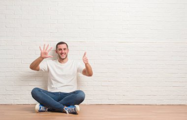 Gösterilen ve parmakları ile işaret beyaz tuğla duvarın üzerinden katta oturan genç beyaz adam kendinden emin ve mutlu gülümseyerek süre 6 numara.