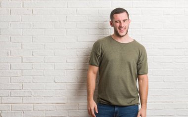 Genç beyaz adam seksi bir ifadeyle, neşeli ve mutlu yüzünü kameraya bakarak göz kırpıyor beyaz tuğla duvarın üzerinden ayakta.