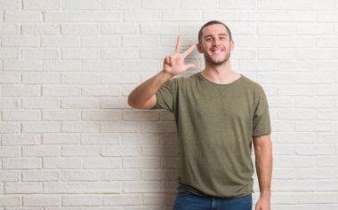 Beyaz delikanlı gösterilen ve parmakları ile işaret beyaz tuğla duvarın üzerinden ayakta üçüncü ise kendinden emin ve mutlu gülümseyerek.