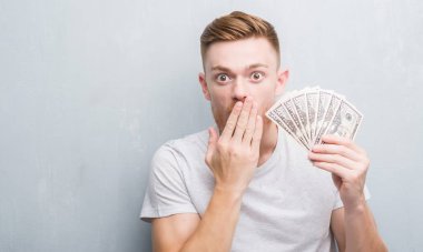 Genç Kızıl saçlı adam dolar kapağı ağız el hata, korku, sessizlik içinde gizli kavramı korkmuş ifade için utanç ile şok ile tutarak gri grunge duvarın üzerinden