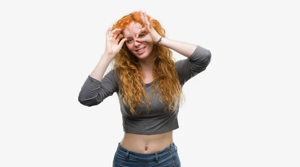 年轻红头发的妇女做 手势用手微笑 眼睛看通过手指与愉快的面孔 — 图库照片
