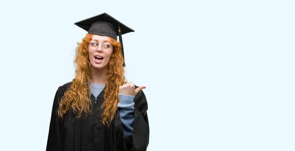 Joven Estudiante Pelirroja Vistiendo Uniforme Graduado Señalando Mostrando Con Pulgar — Foto de Stock