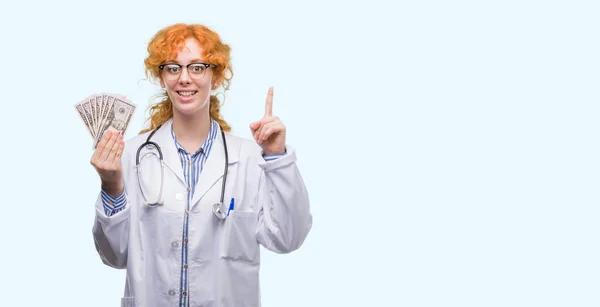 Jovem Médica Ruiva Segurando Dólares Surpreso Com Uma Ideia Pergunta — Fotografia de Stock