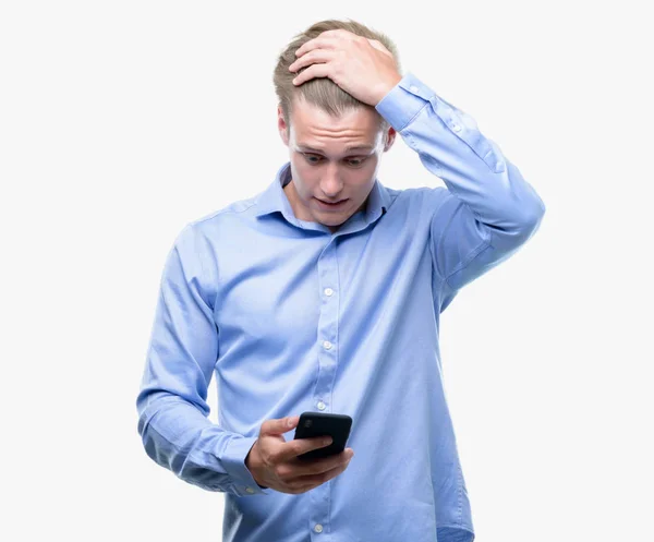 年轻英俊的金发男子使用智能手机强调与手在头上 惊讶的羞愧和惊喜的脸 愤怒和沮丧 对错误的恐惧和不安 — 图库照片