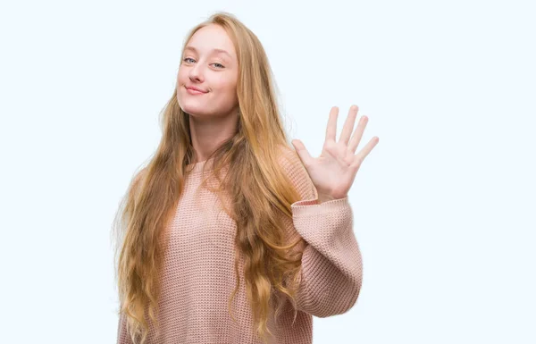 指で上向きの表示とピンクのセーターを着ている金髪 代女性数は自信を持って 幸せな笑みを浮かべている間 — ストック写真