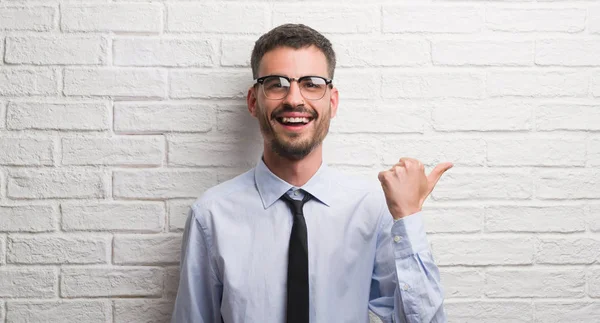 年轻的商业男子站在白色砖墙指向和显示与拇指到一边 快乐的脸微笑着 — 图库照片