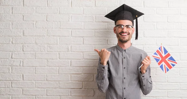 Homem Adulto Jovem Sobre Parede Tijolo Usando Tampa Graduação Segurando — Fotografia de Stock