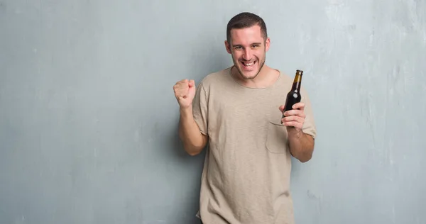 Young Caucasian Man Grey Grunge Wall Holding Bottle Beer Screaming — Stock Photo, Image