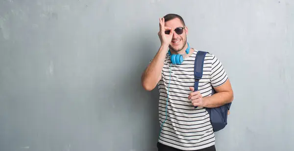 Młody Student Kaukaski Mężczyzna Szary Mur Noszenie Słuchawek Plecak Szczęśliwy — Zdjęcie stockowe