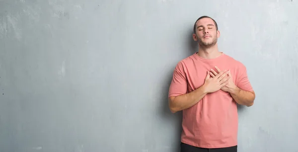 年轻的白种人在灰色的垃圾墙上微笑着双手在胸前闭上眼睛和感激的姿态在脸上 健康理念 — 图库照片