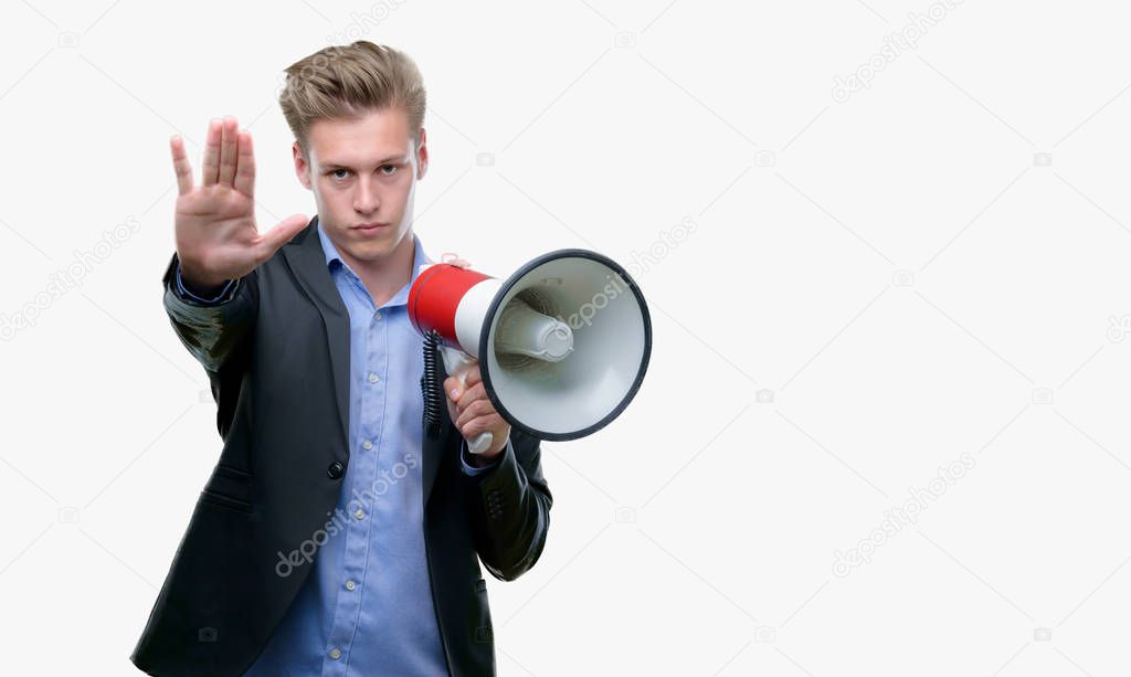 Young handsome blond man holding a megaphone with open hand doing stop sign with serious and confident expression, defense gesture