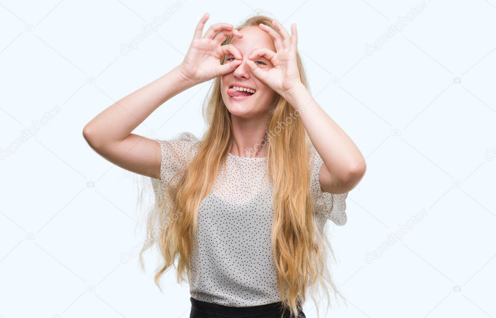 Blonde teenager woman wearing moles shirt doing ok gesture like binoculars sticking tongue out, eyes looking through fingers. Crazy expression.