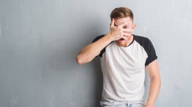 Mahcup ifadeyle parmaklarımın arasından görünen yüz ve gözler el ile kapsayan şok duvar gri grunge bakmak üzerinde genç Kızıl saçlı adam.