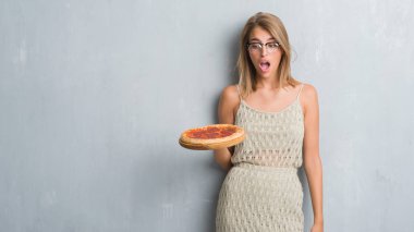 Pepperoni pizza bir sürpriz yüz, korkuyor ve heyecanlı korku ifadesi ile şok korkmuş yemek grunge gri duvar güzel genç kadın