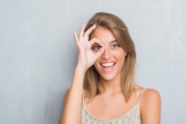 Güzel genç kadın mutlu yüz el parmaklarının arasından seyir göz üzerinde ok işaretiyle yapıyor gülümseyen grunge gri duvardan ayakta