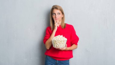 Güzel genç kadın pop corn ciddi bir yüz düşünme hakkında soru, çok karışık fikir yeme grunge gri duvarın üzerinden