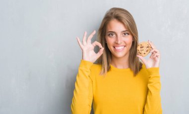 Grunge güzel genç kadın gri ok işareti parmaklar, mükemmel sembolü ile yapıyor çikolatalı bisküvi yemek duvar