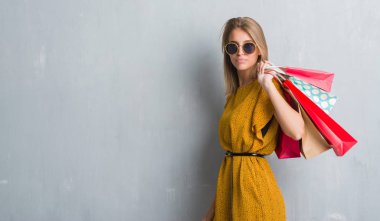 Grunge gri duvar acımak yüz ciddi düşünüyorum üstünde kendine güvenen bir ifade ile satış alışveriş torbaları tutan güzel genç kadın