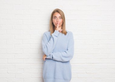 Dudaklarında parmak ile sessiz olmanı beyaz tuğla duvarın üzerinden güzel ve genç birbayan. Sessizlik ve gizli kavramı.