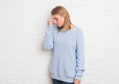 Güzel genç kadın beyaz tuğla duvarın üzerinden sürtünme burun ve göz yorgunluğu ve baş ağrısı duygu yorgun. Stres ve hayal kırıklığı kavramı.