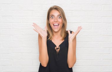 Beyaz tuğla duvar çok mutlu ve heyecanlı, kazanan ifade büyük gülümseme ile çığlık ve ellerini kaldırdı zaferini kutluyor güzel genç kadın