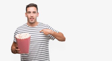 Yakışıklı genç adam yeme patlamış mısır sürpriz yüz işaret parmağı kendisine