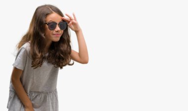 Esmer Latin kız çok mutlu ve gülümseyen uzakta el ile üzerine kafa seyir güneş gözlüğü takıyor. Arama kavramı.
