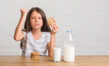 Süt ve çikolata bisküvi rahatsız yeme ve öfke, çılgın ve yükseltilmiş el, öfke kavramı ile diye bağıran ile sinirli bağırarak içme masada oturan genç İspanyol çocuk