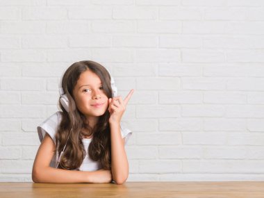 Kulaklıklar el ve parmak ile tarafına işaret çok mutlu giyen masada oturan genç İspanyol çocuk