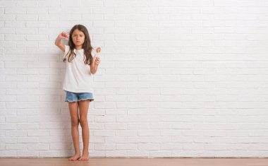 Lolipop şeker evde kızgın yüzü, eksi işareti aşağı antipati başparmak ile gösterilen, ret kavramı ile beyaz tuğla duvarın üzerinden genç İspanyol çocuk