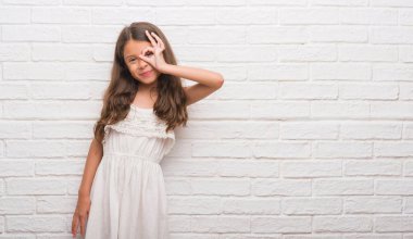 Genç İspanyol çocuğun gülümseyen, parmakları ile mutlu yüz üzerinden seyir göz el ile ok jest yapıyor beyaz tuğla duvarın üzerinden.