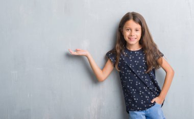 Grunge gri duvar neşeli sunulması ve kameraya bakarak avucunun ile işaret gülümseyen genç İspanyol çocuk.