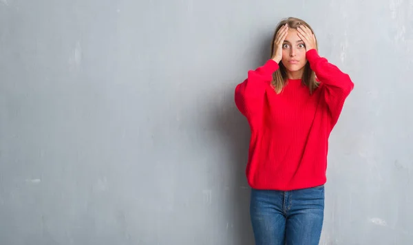 Beautiful young woman standing over grunge grey wall wearing winter sweater stressed with hand on head, shocked with shame and surprise face, angry and frustrated. Fear and upset for mistake.