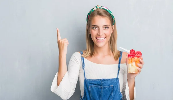 グランジに美しい若い女性食べるアイデアに驚いて壁をグレーや幸せそうな顔 ナンバーワンと人差し指の質問 — ストック写真