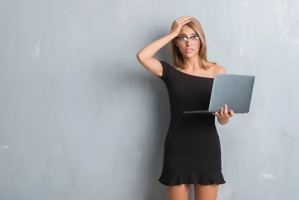 Beautiful young business woman over grunge grey wall using computer laptop stressed with hand on head, shocked with shame and surprise face, angry and frustrated. Fear and upset for mistake.