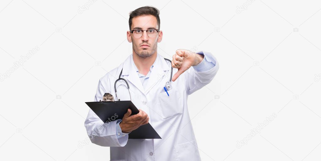 Handsome young doctor man holding a clipboard with angry face, negative sign showing dislike with thumbs down, rejection concept