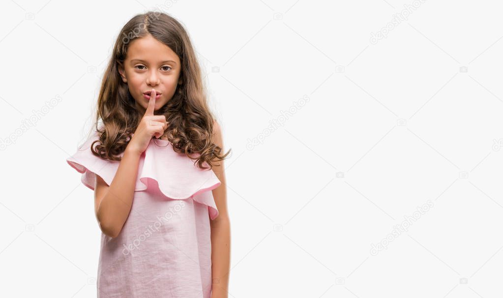 Brunette hispanic girl wearing pink dress asking to be quiet with finger on lips. Silence and secret concept.